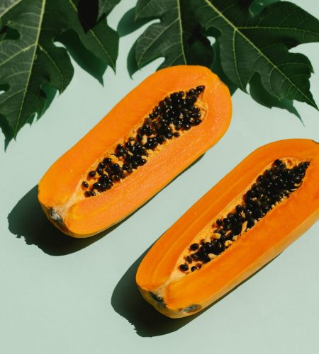 From above composition of green leaves and halved tasty papaya with seeds placed on green background and casting shadow